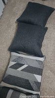 Three dark solid color sofa pillows with textured fabric and one geometric pattern pillow displayed on carpeted floor.