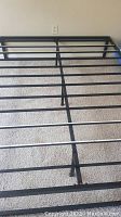Black metal queen bed frame showing top view of slats and central support legs on carpeted floor