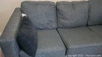 Front view of dark gray sofa with three back cushions and a black square pillow on left arm.
