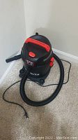 Front view of black and red Stealth wet/dry vacuum cleaner showing attached hose, power cord, and handle on top