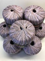 Top-down view of seven tightly wound yarn balls stacked showing the multicolor strands in muted lilac/pink, pale grey and coffee tones.