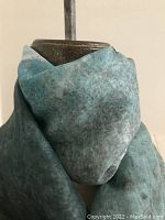 Silk scarf wrapped around a dress form, showing rich turquoise and grey tones and soft texture.