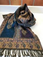 Image showing the scarf loosely rolled with visible swirling pattern and vivid blue, eggplant, and amber colors with fringe.