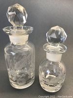 Front view of the two etched crystal containers showing the faceted stoppers and engravings.