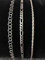 Three sterling silver bracelets with varied chain designs displayed on black fabric background