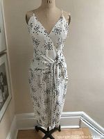 Dress displayed on a dress form showing front view of knee-length cream cross over dress with black polka dots and waist tie.