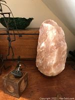 Photo showing the Himalayan salt lamp placed on a wooden surface with surrounding decorative items, highlighting the lamp's natural crystalline salt texture and wooden base.