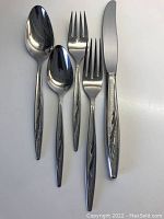Close-up photo showing individual dinner knife, dinner fork, dessert fork, soup spoon, and teaspoon with detailed abstract long leaf handles.