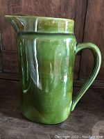 Front view of the forest green handmade clay pitcher, showing the spout, handle, and overall shape.