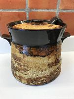 Front view of the glazed clay serving pot with lid on, showing textured finish and dark brown glazed top rim and handles.