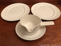 Top-down photo of two oval small meat platters, one gravy boat, and one saucer showing the textured linear detail on the rim and sides under warm lighting on wooden surface.