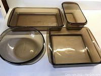Photo showing all four pieces of smoky coffee colored Pyrex bakeware including rectangular, square, round, and smaller rectangular dishes on a white background