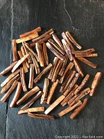 Overview of 52 dyed amber colored mother of pearl twig-shaped beads scattered on a dark surface, showing size and shape variety.