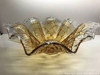 Rippled amber Murano glass bowl with flower-like edges viewed from side showing rippled contours and linear darker amber abstract checkered pattern in clear glass.