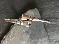 Close-up of the bangle showing the two closed fist ends and surface etched decoration on the band.