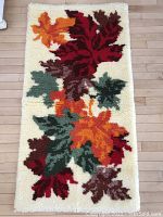 Full view of rectangular vintage hand hooked rug, showing multicolored autumn leaves in red, orange, green and brown on a creamy background, placed on light wooden floor.