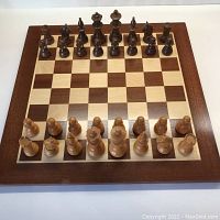 Full view of chess pieces set up on wooden chess board showing alternating dark and light squares with mitered corner frame