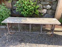 Front view of a weathered vintage locker room bench with wood top and metal wire cage storage compartments underneath. Shows overall structure and wire mesh sections.
