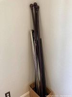 Dark bronze curtain rods with round knobs clustered in a box, several rods visible leaning against a wall.