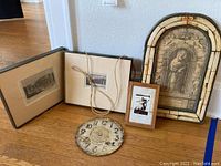 Wide shot of all items: four framed art pieces and one unframed, two clock faces on floor.