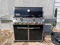 Front view of black and stainless steel grill with control knobs, side shelves, cabinet doors, and folded black cover visible on right