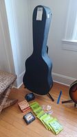 Guitar hard case on stand with various guitar strings and picks laid out on floor.