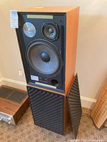 Single speaker with front grille removed showing woofer, midrange and tweeter