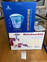 Boxes of KitchenAid Metal Food Grinder attachment and AquaBliss Water Pitcher stacked, showing branding and product images