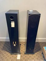 Front and rear view of two black floor-standing speakers with removable cloth grilles and base stands