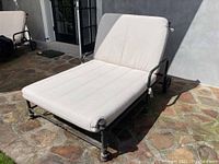 Angled front view of chair on stone patio showing metal frame, cushion, and caster wheel