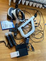 Overall lot including VR headset, Processor Unit, Move controllers, Aim controller, Camera, game disc and cables laid out on wood floor