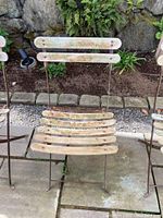 Weathered vintage Parisian cafe chair showing wood slats and rusted metal frame outdoor in garden.