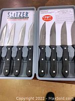 8 Slitzer jumbo steak knives with black ergonomical handles and stainless steel blades in gray plastic case