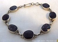 Top view of the sterling silver bracelet showing seven oval rough facetted blue sapphire cabochons set in silver bezels with linked chain and hook closure.