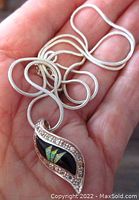 Hand holding a sterling silver necklace chain with a pendant featuring opal inlay, black onyx background, and cubic zirconia stones.