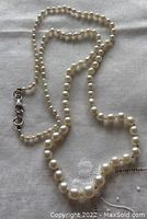 Top view of vintage cultured pearl necklace laid out on white fabric showing pearl gradation and sterling silver lobster clasp.