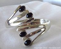 Front side of sterling silver hinged bangle showing four black onyx cabochons and openwork design.