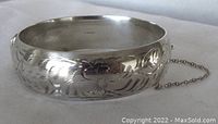 Close-up front view of the hinged bangle bracelet showing floral engravings and safety chain.