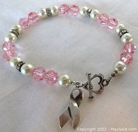 View of vintage sterling silver bracelet with faux pearls, pink glass beads, silver rhinestone spacers and a ribbon-shaped charm on a heart toggle clasp.