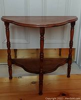 Front view of a walnut D-shaped end table showing turned legs and lower shelf.