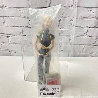 Full view of Britney Spears doll sealed inside original clear plastic bag. Doll dressed in black and yellow outfit, standing upright.