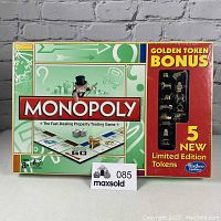 Front view showing Monopoly board game with Golden Token Bonus featuring 5 new limited edition gold-colored tokens visible through window in sealed packaging.