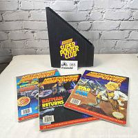 Photo showing three Nintendo Power magazines with vibrant front covers and a black display holder with yellow Super Power Club logo.