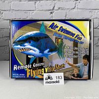 Box front showing branding Remote Control Flying White Shark, labeled Air Swimming Fish, 57 inches long, with image of shark and people.