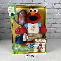 Front view of Sesame Street Check-Up Time Elmo plush toy in original packaging showing Elmo with medical accessories including stethoscope, medical bag, syringe, and bandage.