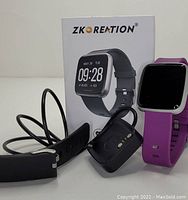 Photo shows Zkoreation smartwatch with black and purple bands and charging cables alongside the original box.