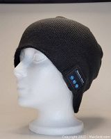 Side view of a black tight fitting knitted touque displayed on a mannequin head. Shows integrated Bluetooth control panel with buttons labeled for music and calls.