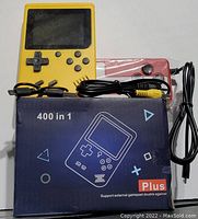 Yellow handheld game console with D-pad, buttons, screen, red secondary controller, and cables in front of the packaging box labeled "400 in 1"
