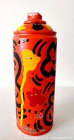 Front view of spray can sculpture showing orange background with orange, black, yellow and red abstract street art.