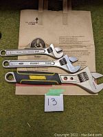 Three adjustable wrenches laid on a brown paper bag, showing various brand markings and sizes.